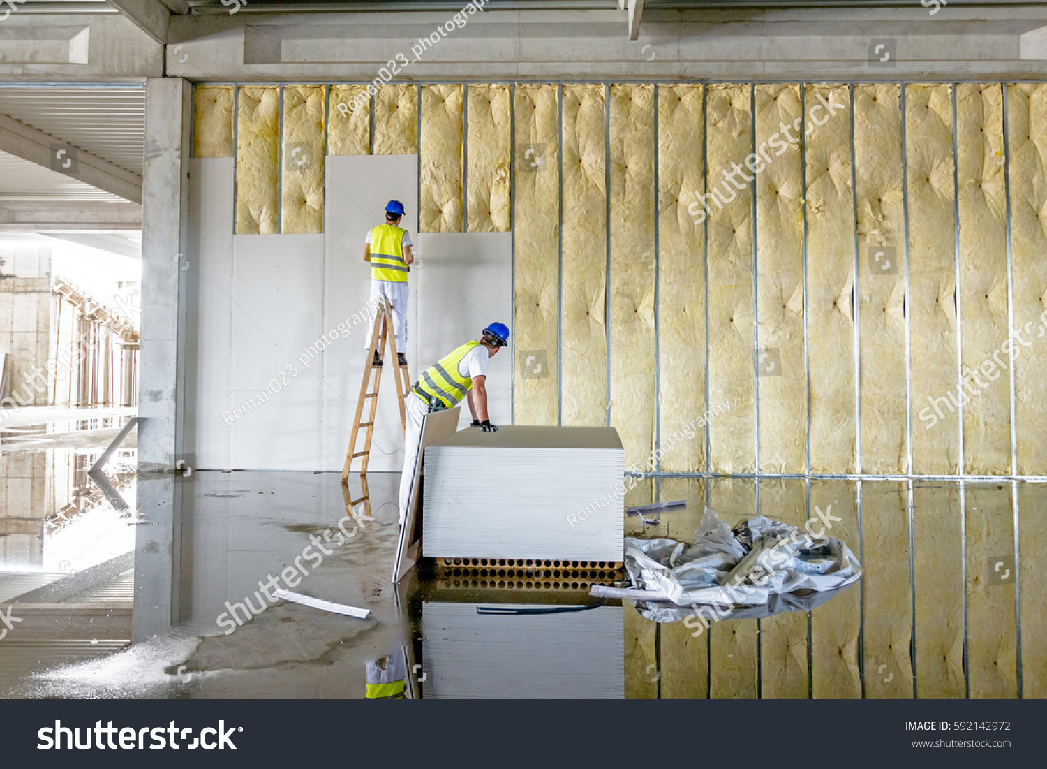 stock-photo-workers-are-assembly-gypsum-wall-plasterboard-is-under-construction-using-wooden-ladder-592142972